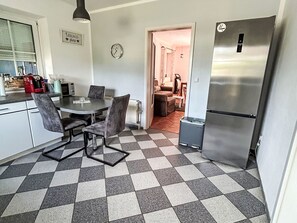 Une cuisine avec un carrelage à motifs, une table à manger avec des chaises, un réfrigérateur et une horloge au mur.