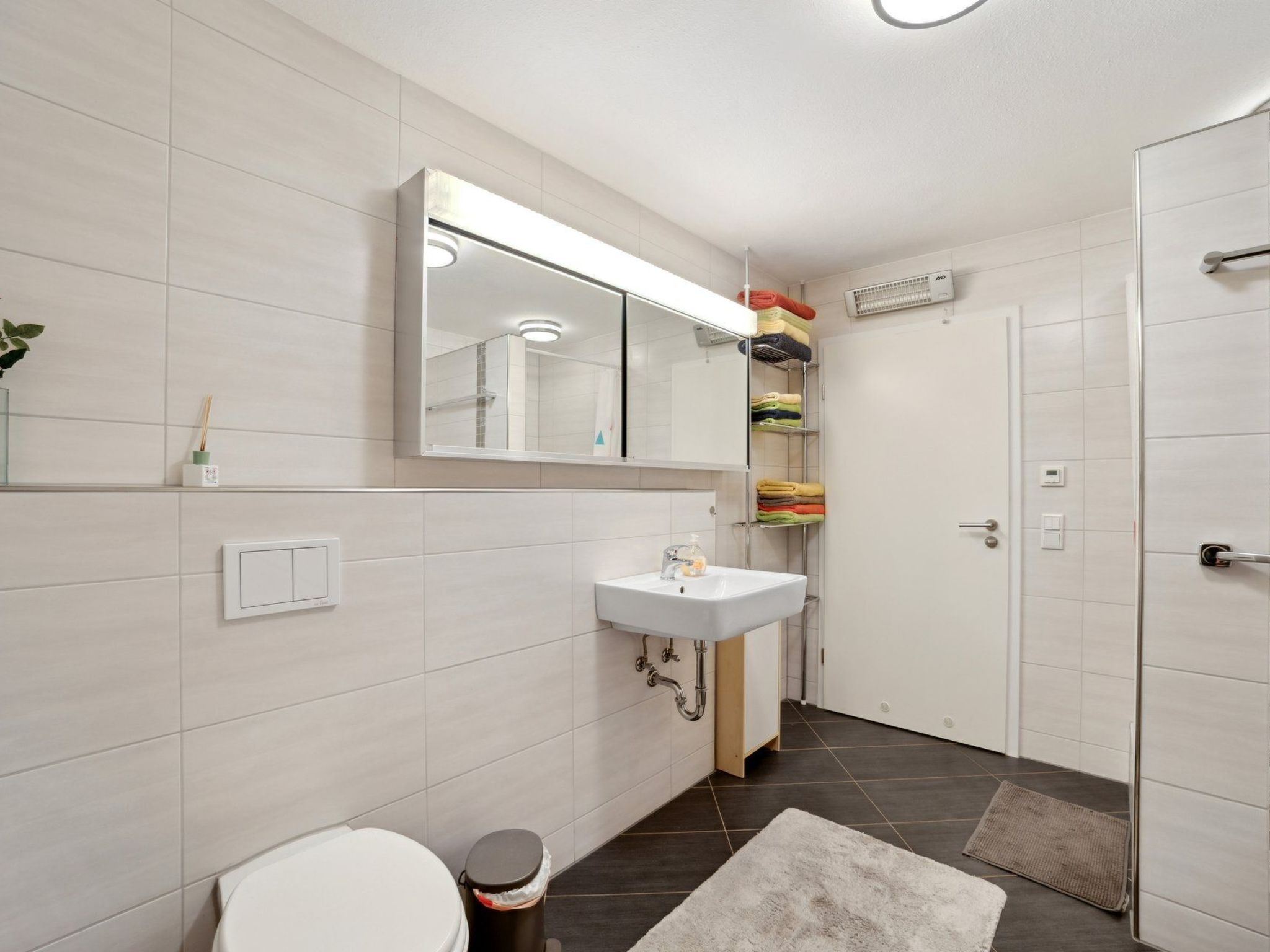 A modern bathroom with a toilet, sink, mirror, and shower area.