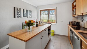 Une cuisine moderne avec un plan de travail en bois, des armoires blanches, un four encastré et une fenêtre donnant sur la forêt.