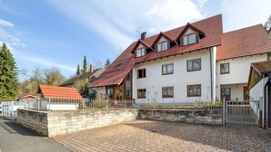 Une maison à deux étages, avec un toit recouvert de tuiles rouges, des murs blancs et un chemin en briques menant à l’entrée.