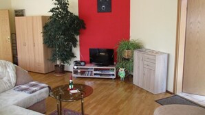 A living room with a red accent wall, a large plant, a TV, and a wooden cabinet. - Appartement in Törten by Interhome (Törten)