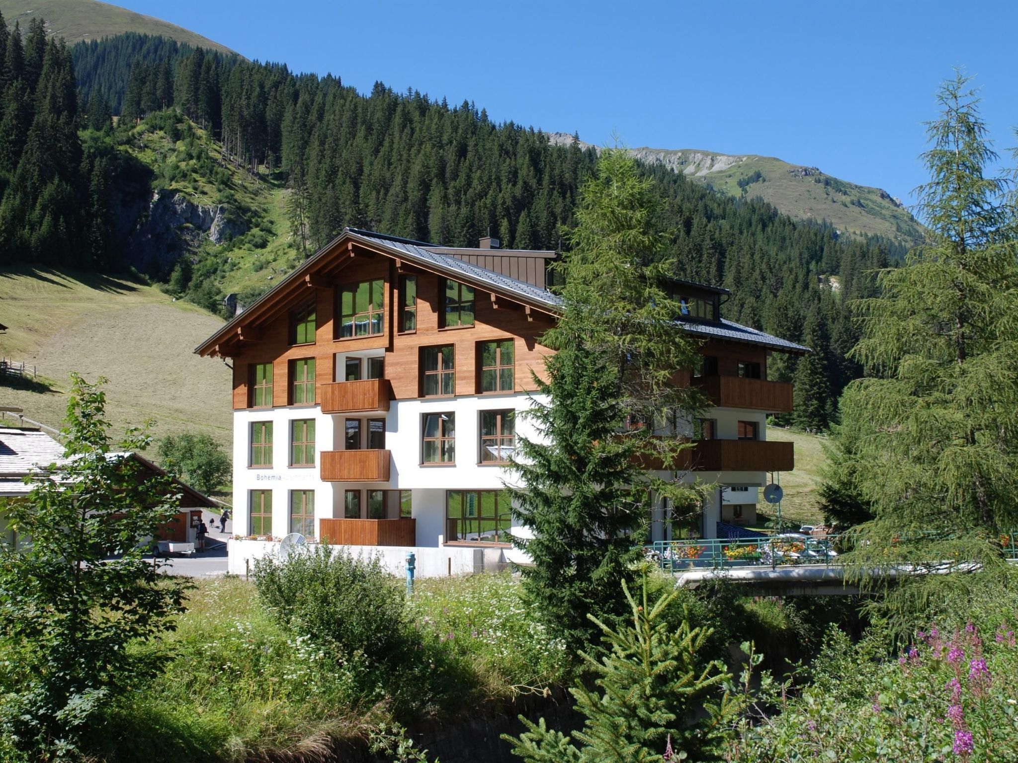 Un immeuble à plusieurs étages doté de balcons, entouré de forêts et de montagnes.