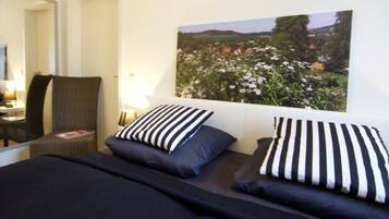 Ein Schlafzimmer mit einem Bett, zwei Kissen, einem Sessel, einem Nachttisch und einem an der Wand hängenden Bild von einem Garten.