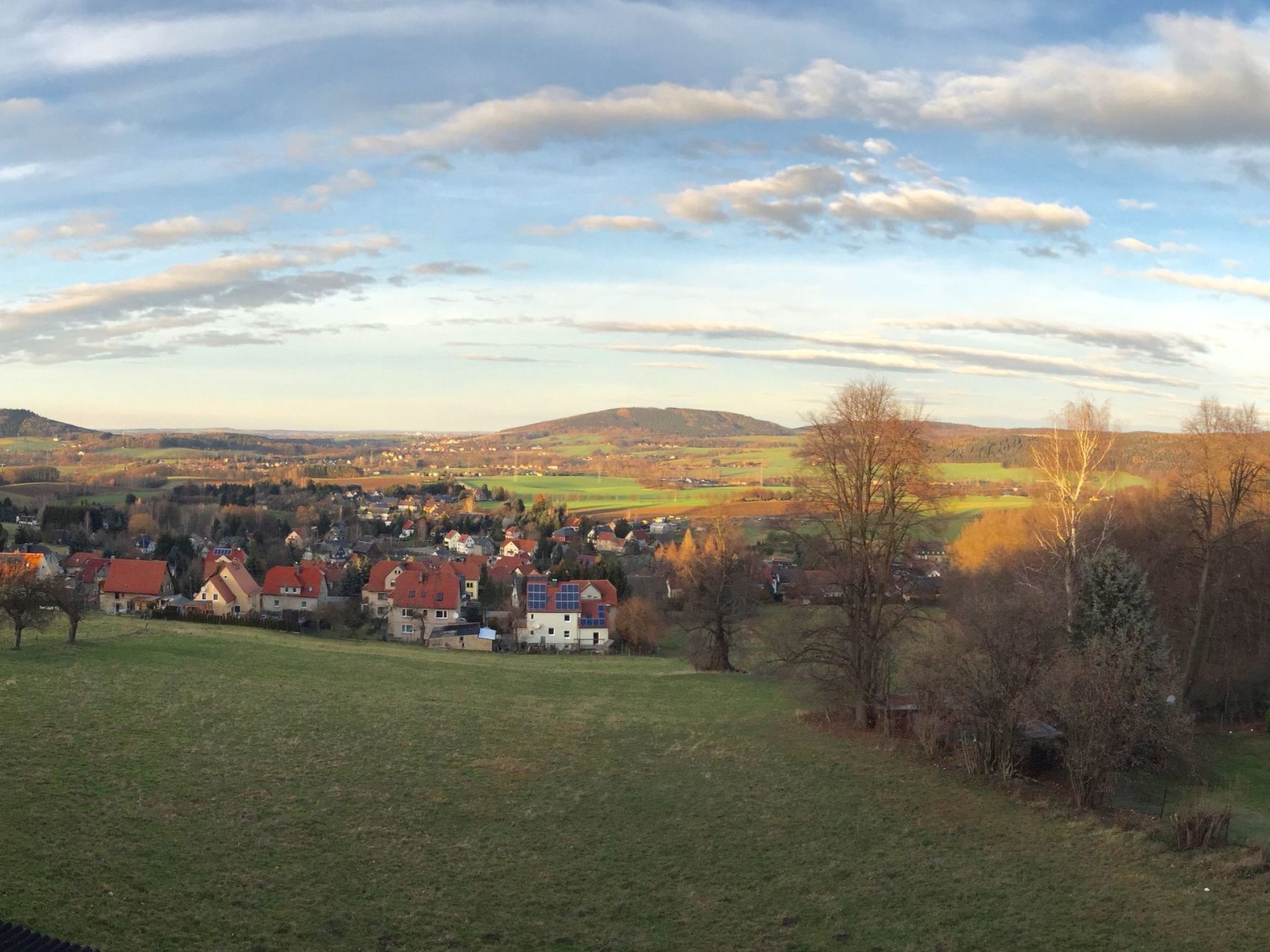 A rural landscape with houses on a hill, a clear sky, and a distant view of fields and hills.