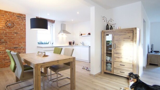 Una cucina moderna con un tavolo e sedie in legno, un muro in mattoni e un cane sdraiato sul pavimento.