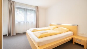A modern hotel room with a wooden bed, a bedside table, and a large window with curtains. - Bohemia 4 in Gargellen by Interhome (Gargellen)