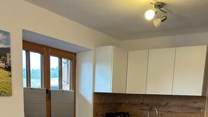 Una cucina moderna con mobili bianchi, un piano di lavoro nero, forno integrato e una finestra con persiane.