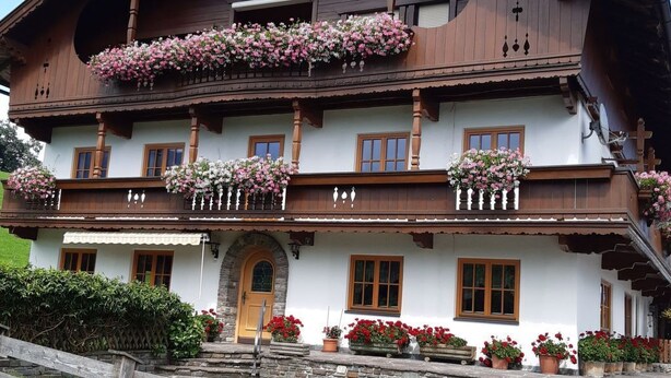 Una casa di legno tradizionale con un balcone, gradini in pietra e vasi di fiori.