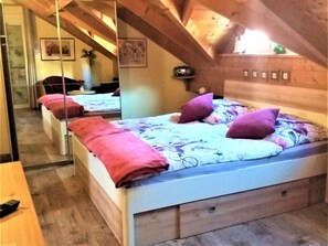A bedroom with a sloped ceiling, wooden beams, a bed with a floral bedspread, and a mirror reflecting the room. - Bergidyll by Interhome (Obertraun)