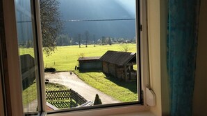 Visão da janela mostrando uma paisagem rural com uma trilha de terra, uma pequena construção de madeira e uma cerca.
