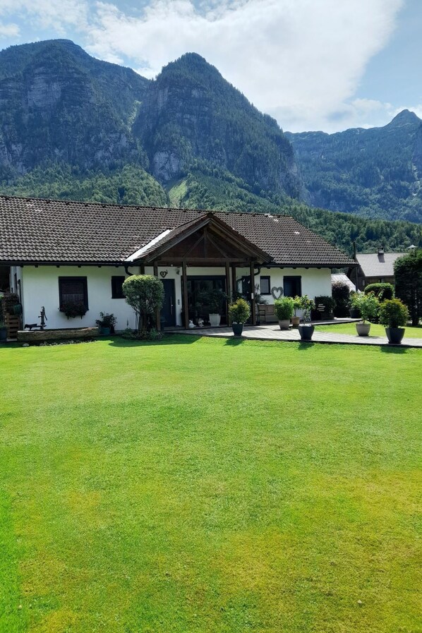 A two-story building with a tiled roof, surrounded by a well-maintained lawn and potted plants. - Bergidyll by Interhome (Obertraun)