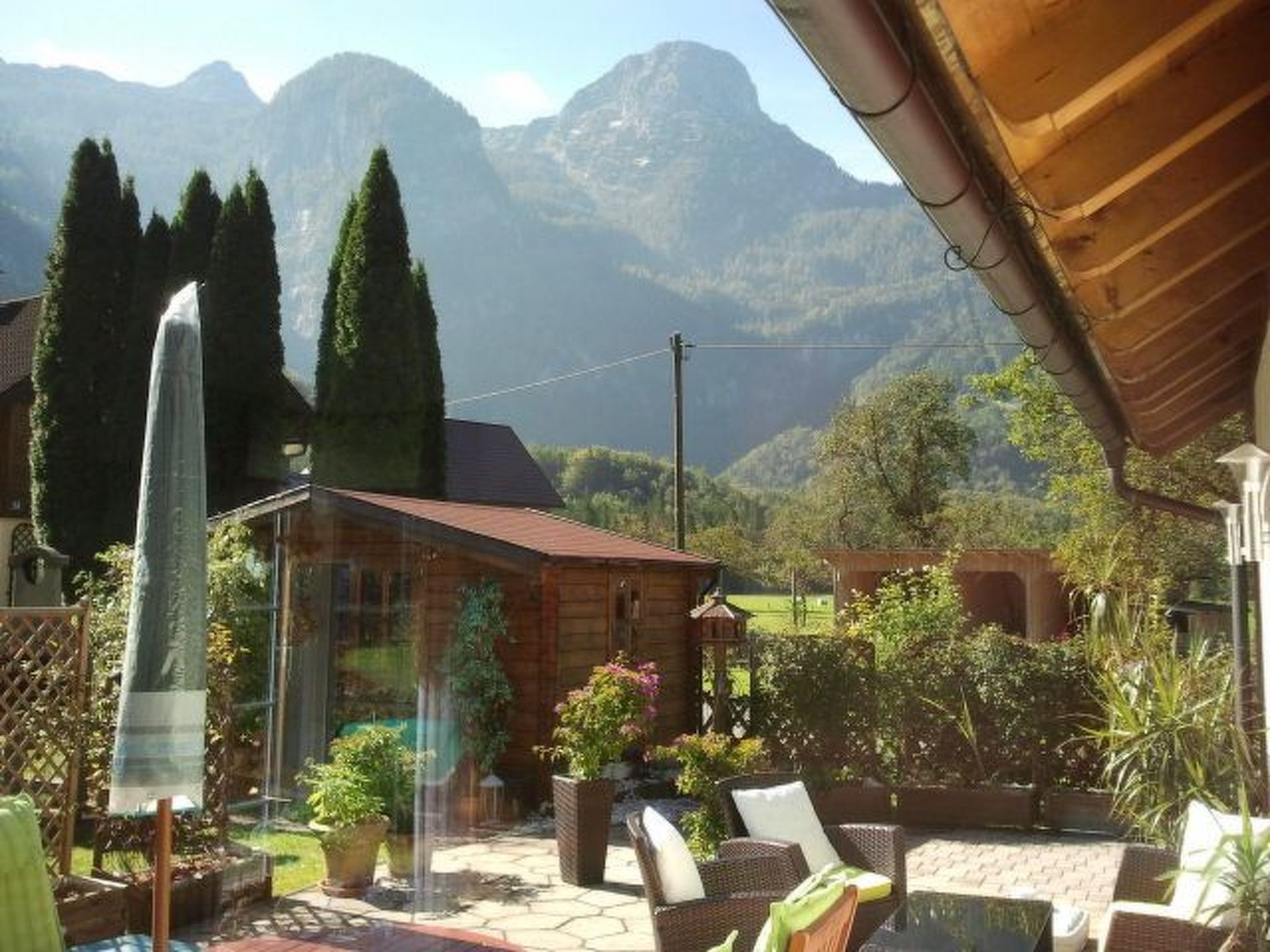 Eine Holzhütte mit Terrasse, umgeben von Topfpflanzen und Blick auf die Berge.