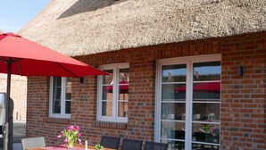 An outdoor patio with a wooden table, chairs, a red umbrella, and a brick building with large windows. - Vacation home Lotte by Interhome (Groß Schoritz)