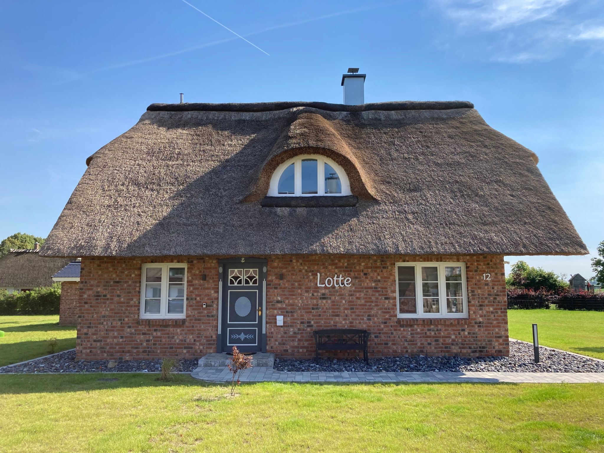 A thatched-roof cottage with a brick facade, a small porch, and a sign reading "Lotte."