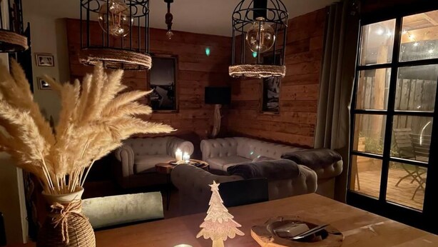 Een gezellige woonkamer met een houten vloer, een bank, een bijzettafeltje met kaarsen en een vaas met pampa's.