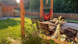 Een terras buiten met houten meubels, een hangmat en een houten pergola.