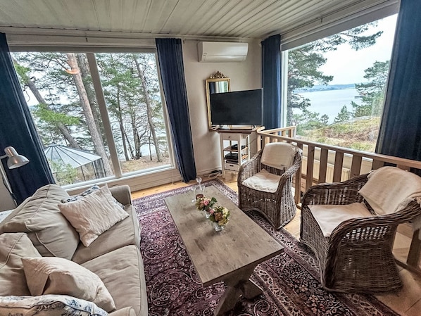 A cozy room with a sofa, a coffee table with flowers, wicker chairs, a TV, and a view of the sea.