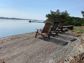 A lakeside seating area with Adirondack chairs and a bench, overlooking a calm lake and distant shoreline.