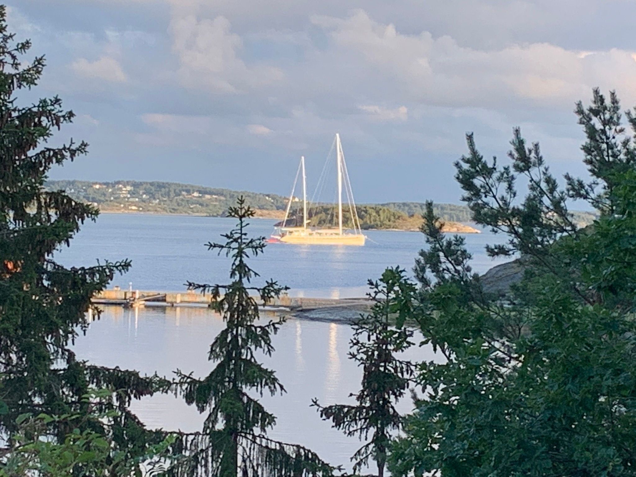 Ein ruhiger See mit einem Segelboot in der Ferne, umgeben von Bäumen und einer Anlegestelle.