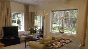 A modern living room with a flat-screen TV, sofa, coffee table, and a large window with a view of trees. - Wunderschönes Cottage "Traum von Wald und Meer" by Interhome (Stenungsund)