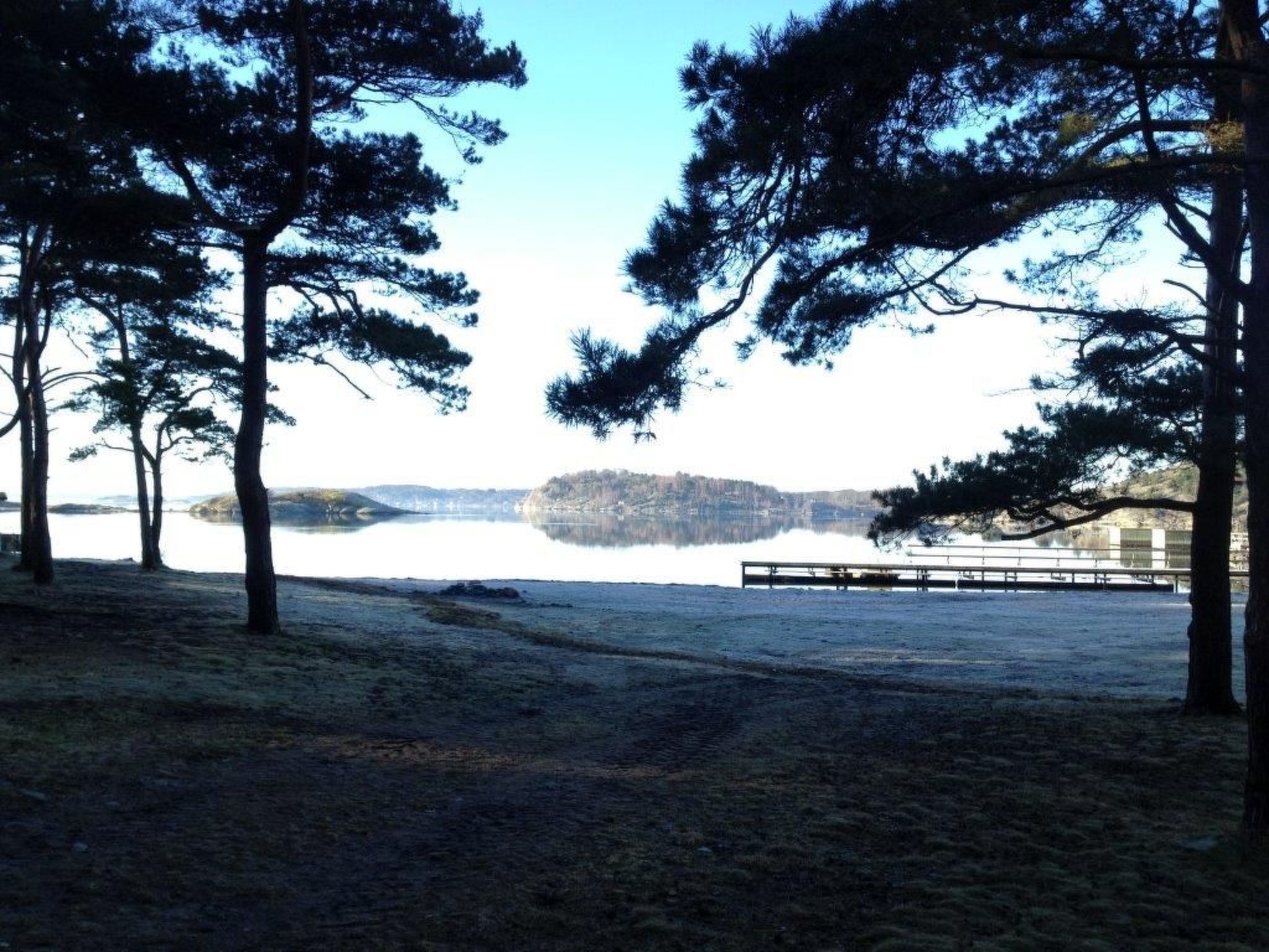 Blick auf einen See mit Bäumen, einem Steg und einer fernen Insel.