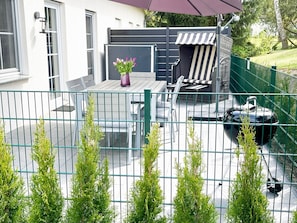 Ein Patio mit Tisch und Stühlen, ein kleiner Garten und ein grüner Zaun.