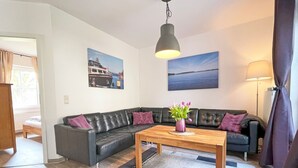 Ett modernt vardagsrum med en svart lädersoffa, ett soffbord i trä och ett stort fönster.