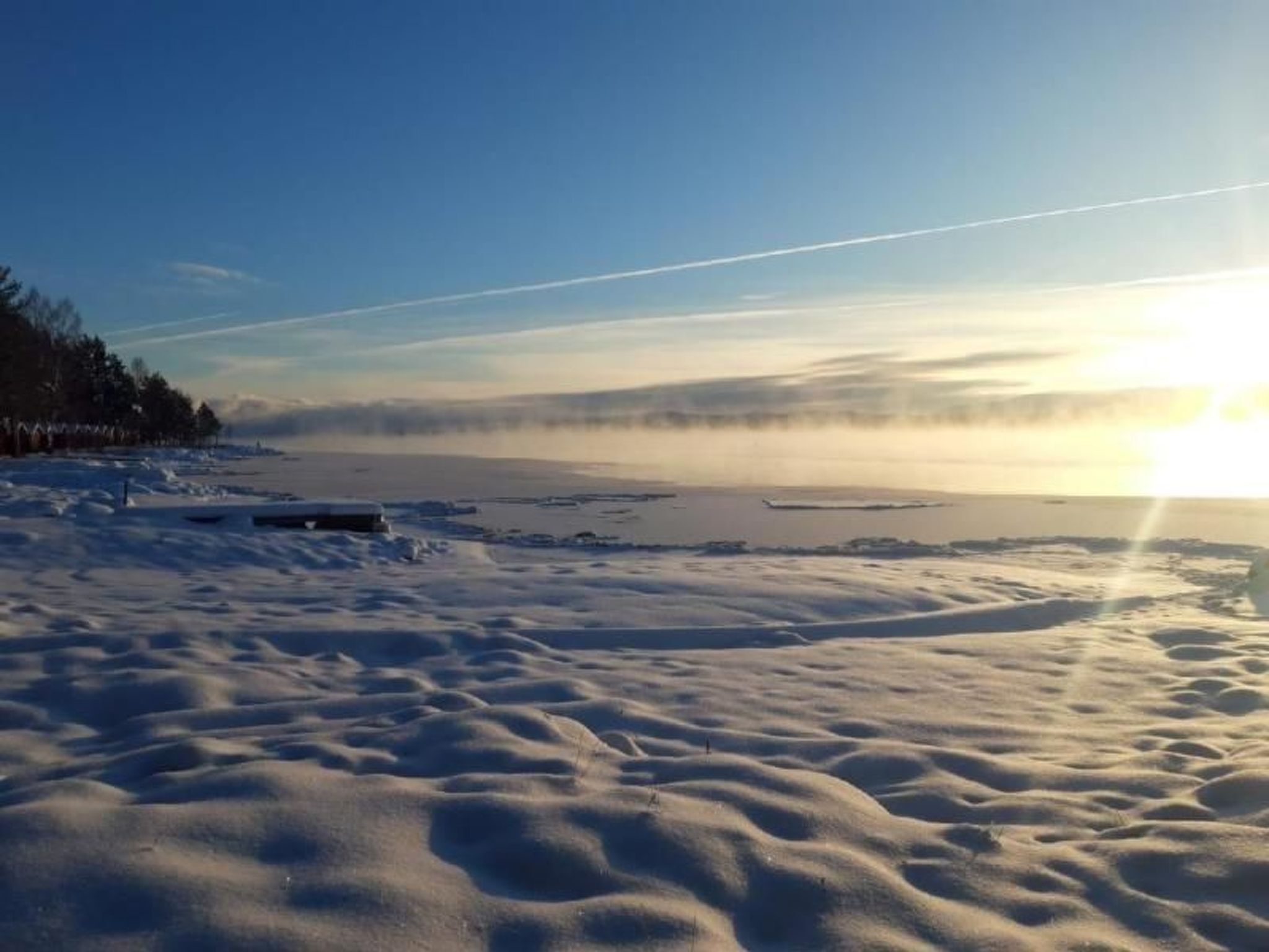 Een besneeuwd landschap met een heldere lucht en een ondergaande of opkomende zon.