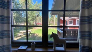 A window with a view of a red building, a white horse statue, and a picnic table outside.