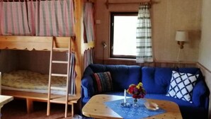 A cozy room with a bunk bed, a blue sofa, a small table with a vase of flowers, and a window with curtains.