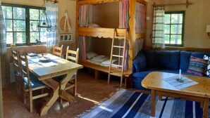 A cozy cabin interior with a bunk bed, a dining table with chairs, a sofa, and a small table with a lamp.