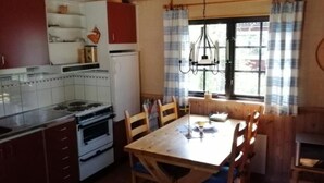 A kitchen with a stove, oven, and cabinets. There is a dining table with chairs and a window with curtains.
