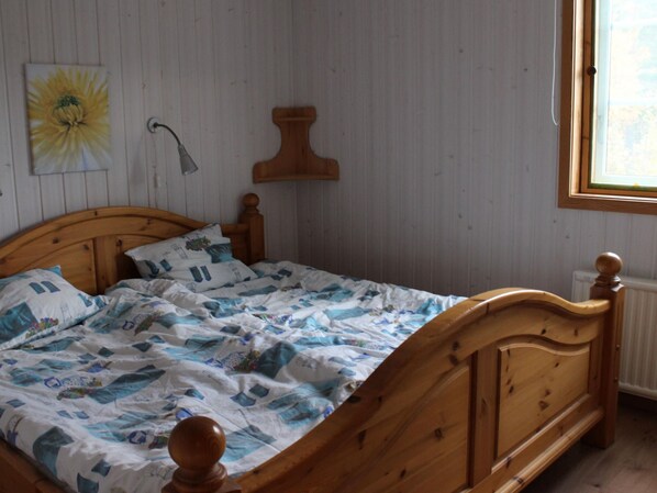 Una cama de madera con colcha de diseño azul y blanco, un cabecero de madera y una lámpara fijada a la pared.