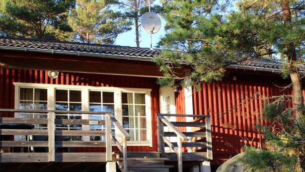 A red cabin with a wooden deck and stairs leading to a window.