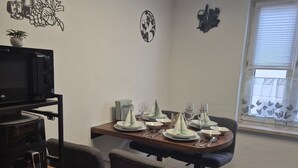 Un coin repas avec une table en bois dressée pour quatre personnes, un four à micro-ondes et une petite plante en pot posée sur une étagère.