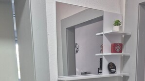 Une salle de bain avec une porte blanche, un miroir et une étagère sur laquelle se trouvent un pot de plante, une boîte rouge et le symbole du Wi-Fi.