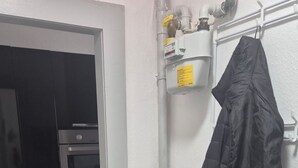 Une cuisine avec un four noir, un réfrigérateur blanc et une étagère blanche sur laquelle est accrochée une veste noire.