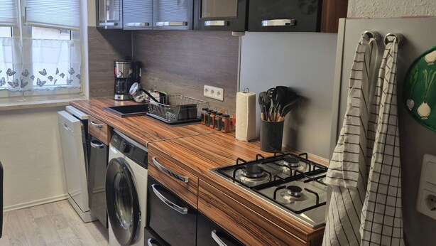 Une cuisine compacte équipée d’un lave-linge, d’une machine à café et d’une cuisinière à gaz.