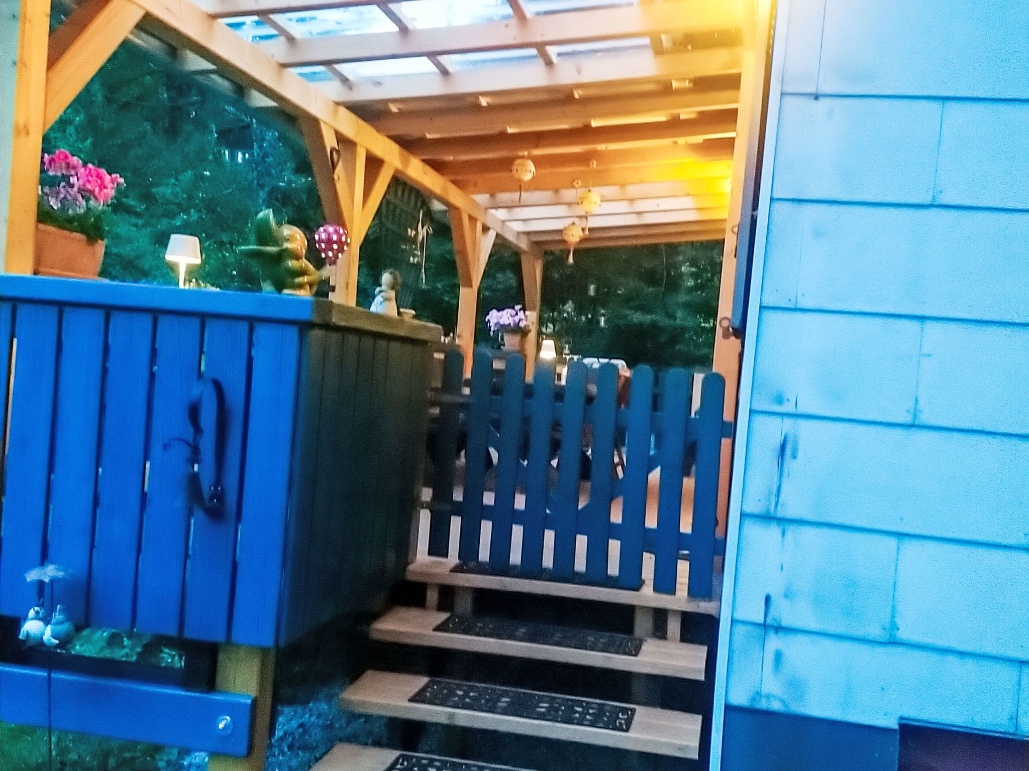 A wooden deck with a blue fence, a small set of steps leading up to a covered area with a glass roof.