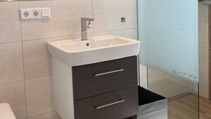 Un bagno moderno con cabina doccia in vetro, un lavabo bianco con mobile scuro e uno specchio sopra il lavabo.