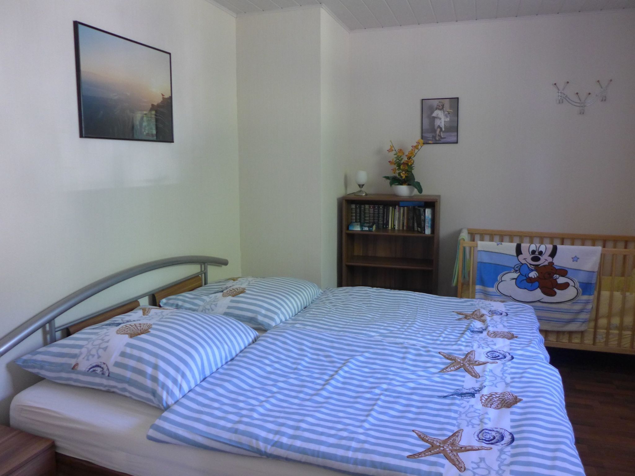 Een slaapkamer met een bed, nachtkastje, boekenkast en ledikant.