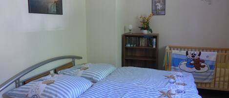 Een slaapkamer met een bed, nachtkastje, boekenkast en ledikant.