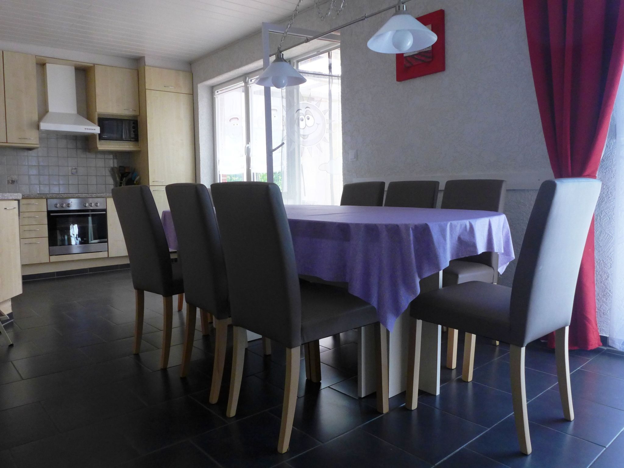 Un coin repas avec une table dressée pour six personnes, entourée de chaises. On peut apercevoir un four à micro-ondes et un four dans la cuisine adjacente.