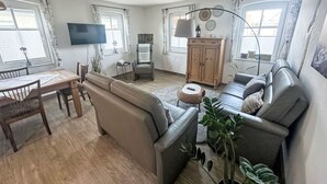 En stue med sofa, spisebord med stole, tv, skab og en plante.