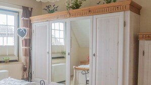 A bedroom with a large white wardrobe, a bed with white bedding, a window with curtains, and a small plant on the windowsill. - Watt in Friedrichskoog-Spitze by Interhome (Friedrichskoog)