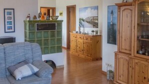 A living room with a grey sofa, a wooden cabinet, and a green tiled fireplace. - Watt in Friedrichskoog-Spitze by Interhome (Friedrichskoog)