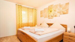 A neatly made bed with pillows and towels, a wooden nightstand with a lamp, and a large floral artwork on the wall. - mit Blick auf das Wasser by Interhome (Geigant)