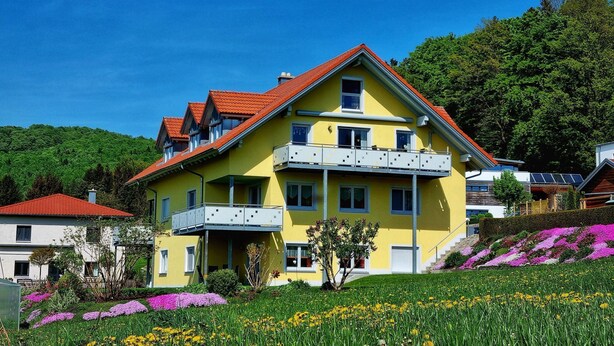 A yellow two-story house with a red roof, a balcony, and a garden with flowers. - mit Blick auf das Wasser by Interhome (Geigant)