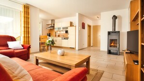 A modern living room with a sofa, a coffee table, and a TV stand. A kitchen is visible in the background with a stove and cabinets. - mit Blick auf das Wasser by Interhome (Geigant)