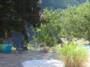 Een terras met een stoel, plantenpotten en een zwembad.